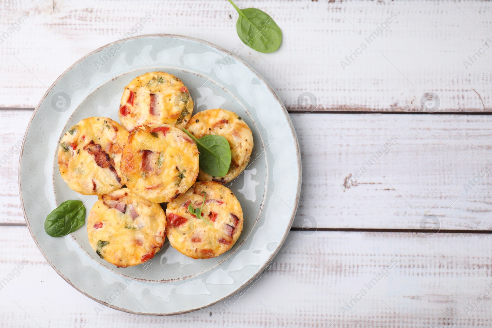 Photo of Delicious egg muffins with cheese and bacon on white wooden table, top view. Space for text
