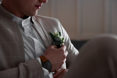 Photo of Groom wearing elegant suit and beautiful boutonniere indoors, closeup view