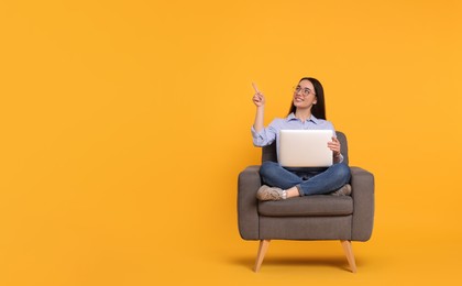 Photo of Smiling young woman with laptop sitting in armchair on yellow background. Space for text