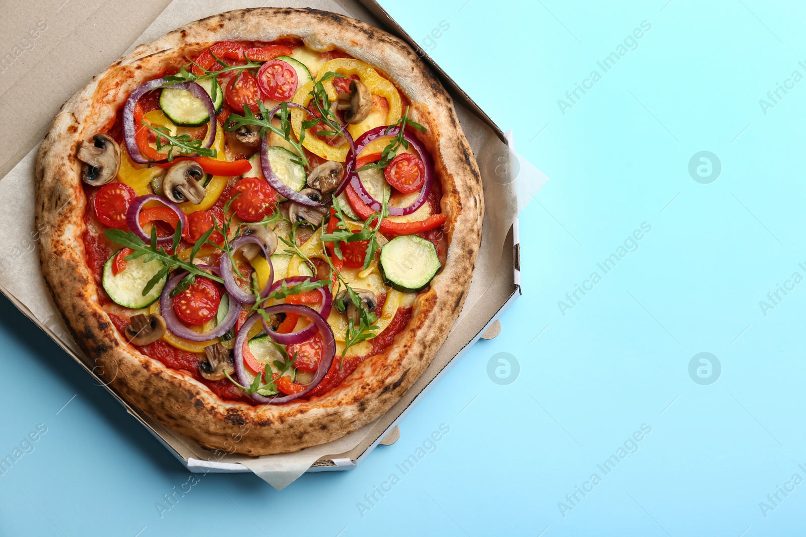 Photo of Delicious hot vegetable pizza in cardboard box on light blue background, top view. Space for text