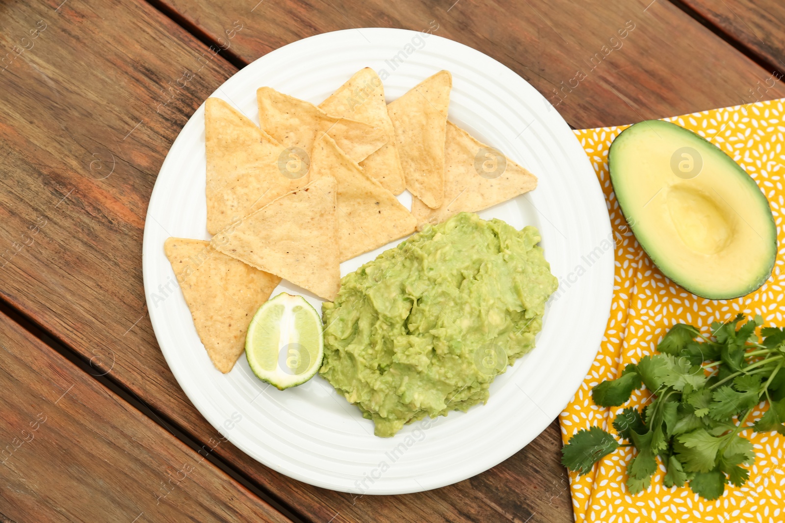 Photo of Delicious guacamole made of avocados, nachos and lime on wooden table, flat lay