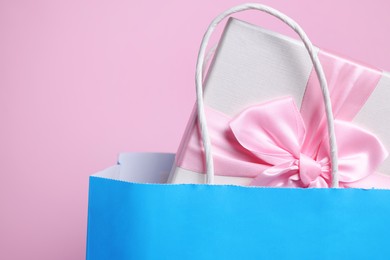 Photo of Light blue paper shopping bag with gift box on pink background, closeup. Space for text