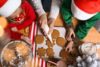 Photo of Mother and her little children decorating tasty Christmas cookies at wooden table, top view