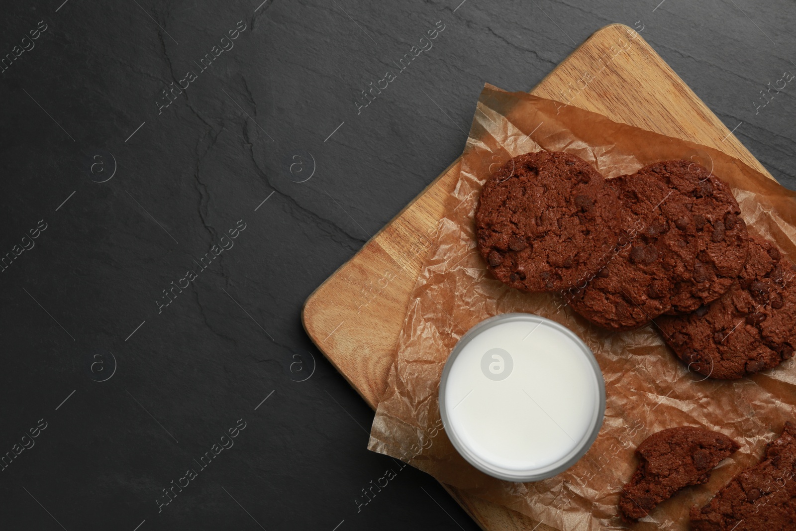 Photo of Board with tasty chocolate cookies and glass of milk on dark table, top view. Space for text