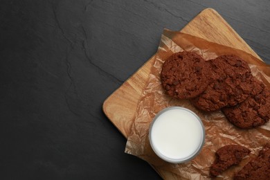 Board with tasty chocolate cookies and glass of milk on dark table, top view. Space for text