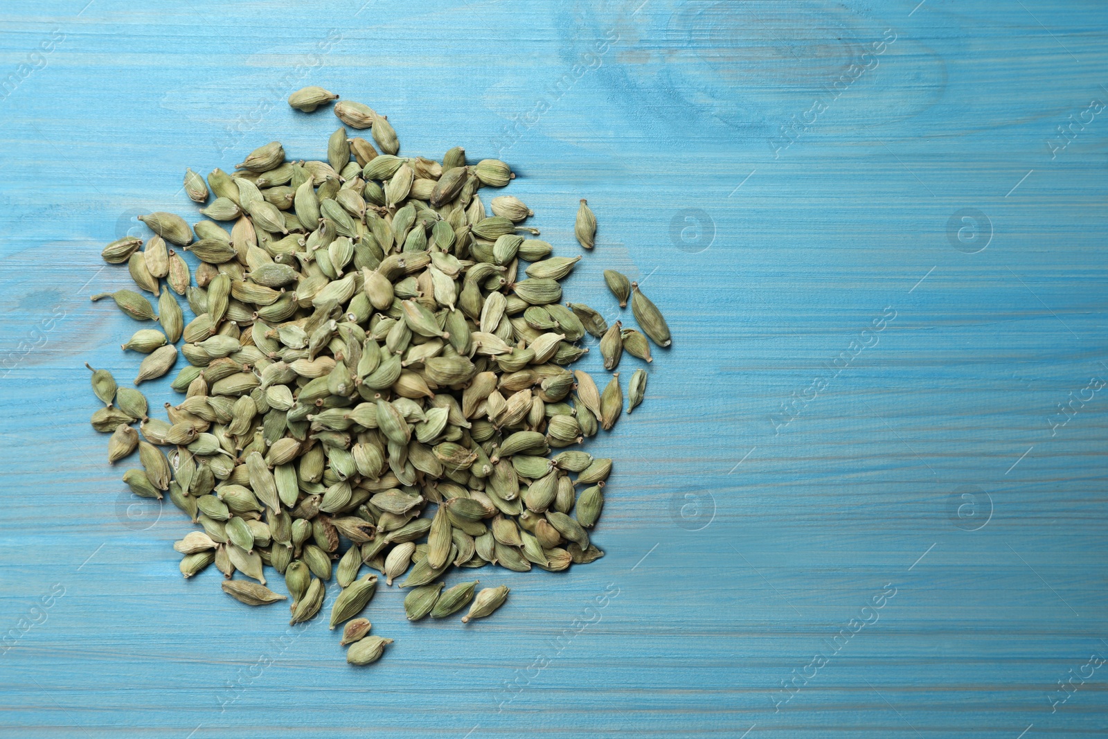 Photo of Pile of dry cardamom pods on light blue wooden table, top view. Space for text