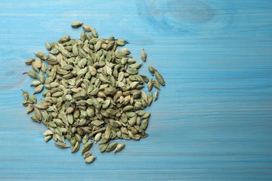 Photo of Pile of dry cardamom pods on light blue wooden table, top view. Space for text