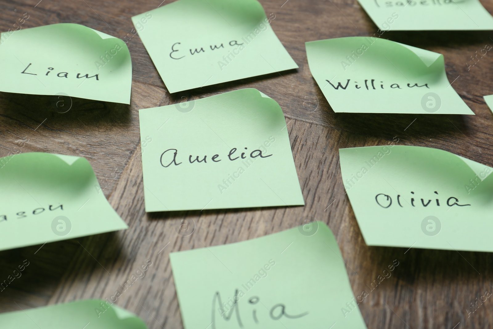 Photo of Paper stickers with different names on wooden table, closeup. Choosing baby's name