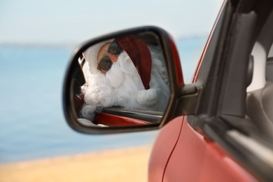 Photo of Authentic Santa Claus looking into side view mirror of car near sea