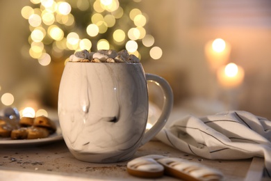 Tasty hot drink with cookies on table against Christmas lights. Space for text