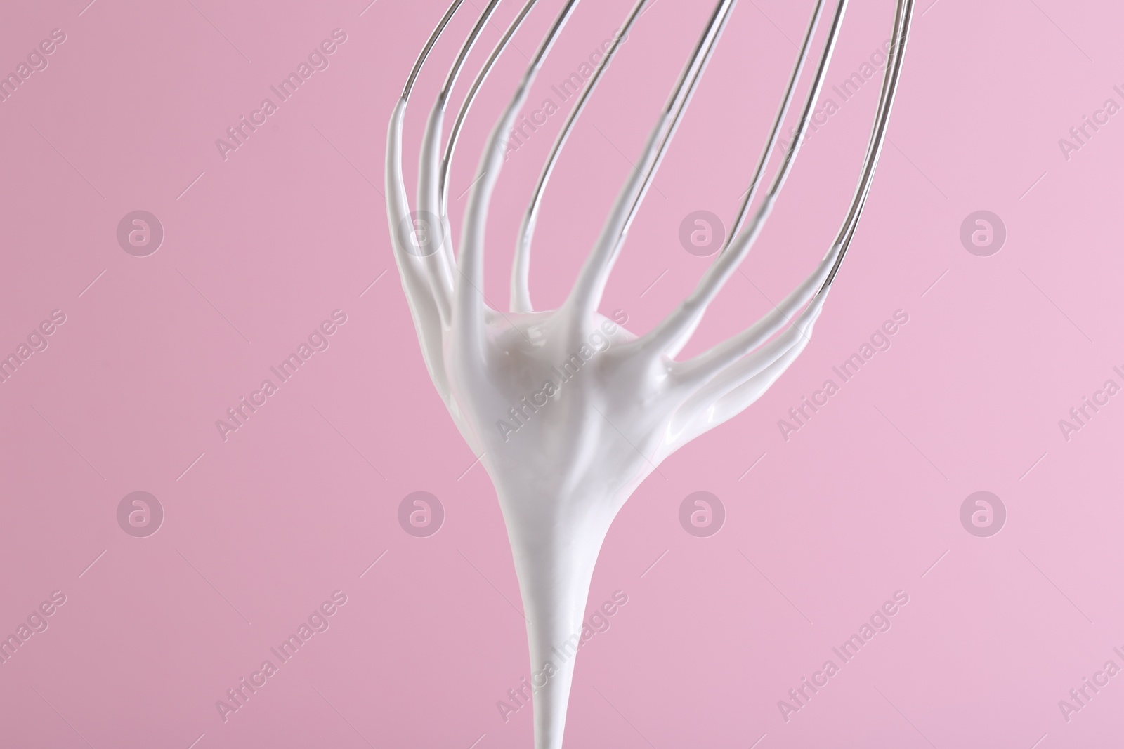 Photo of Whisk with whipped cream on pink background, closeup