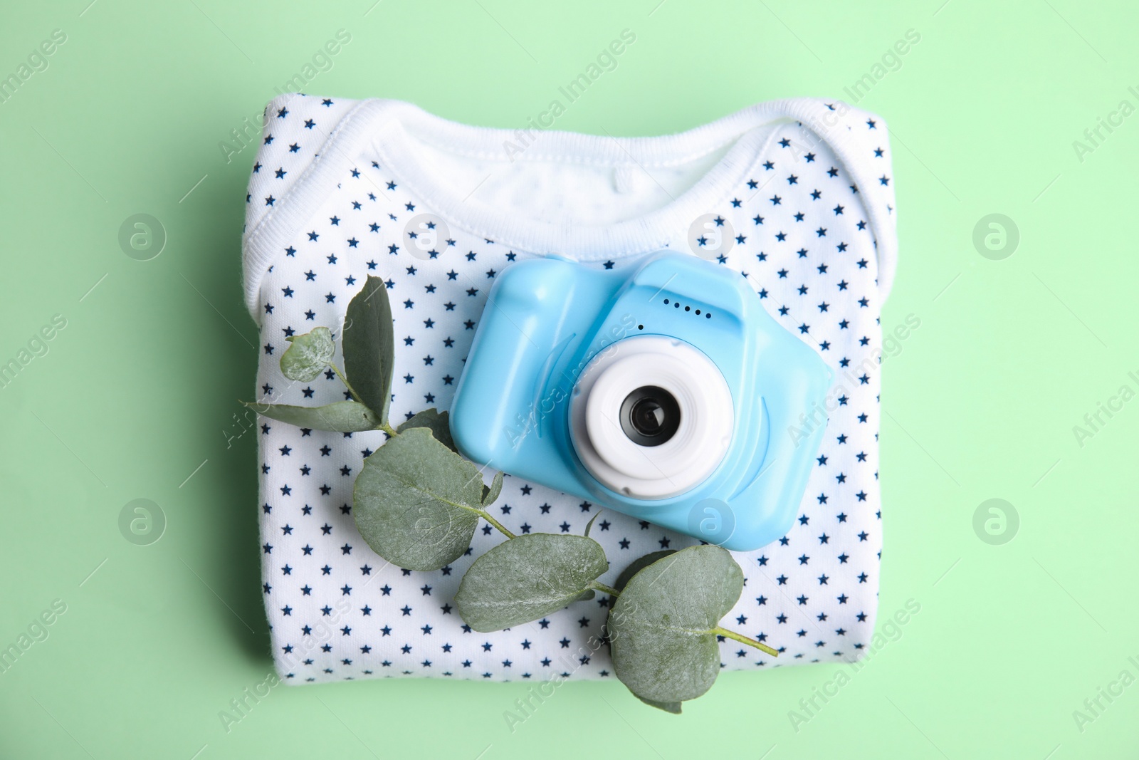 Photo of Toy camera, eucalyptus branch and children's shirt on light green background, top view. Future photographer