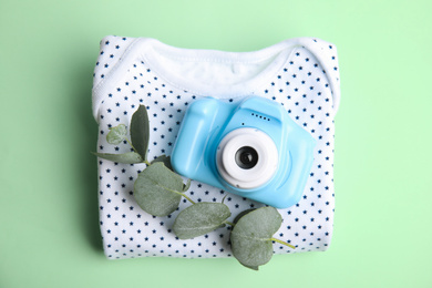 Photo of Toy camera, eucalyptus branch and children's shirt on light green background, top view. Future photographer