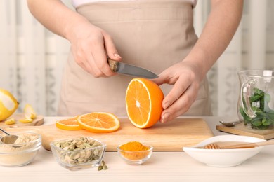 Photo of Woman cutting orange for immunity boosting drink at white wooden table