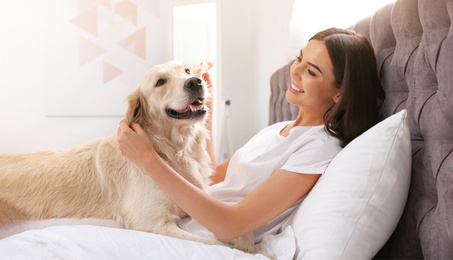 Image of Young woman with her cute Golden retriever on bed at home, banner design. Lovely pet