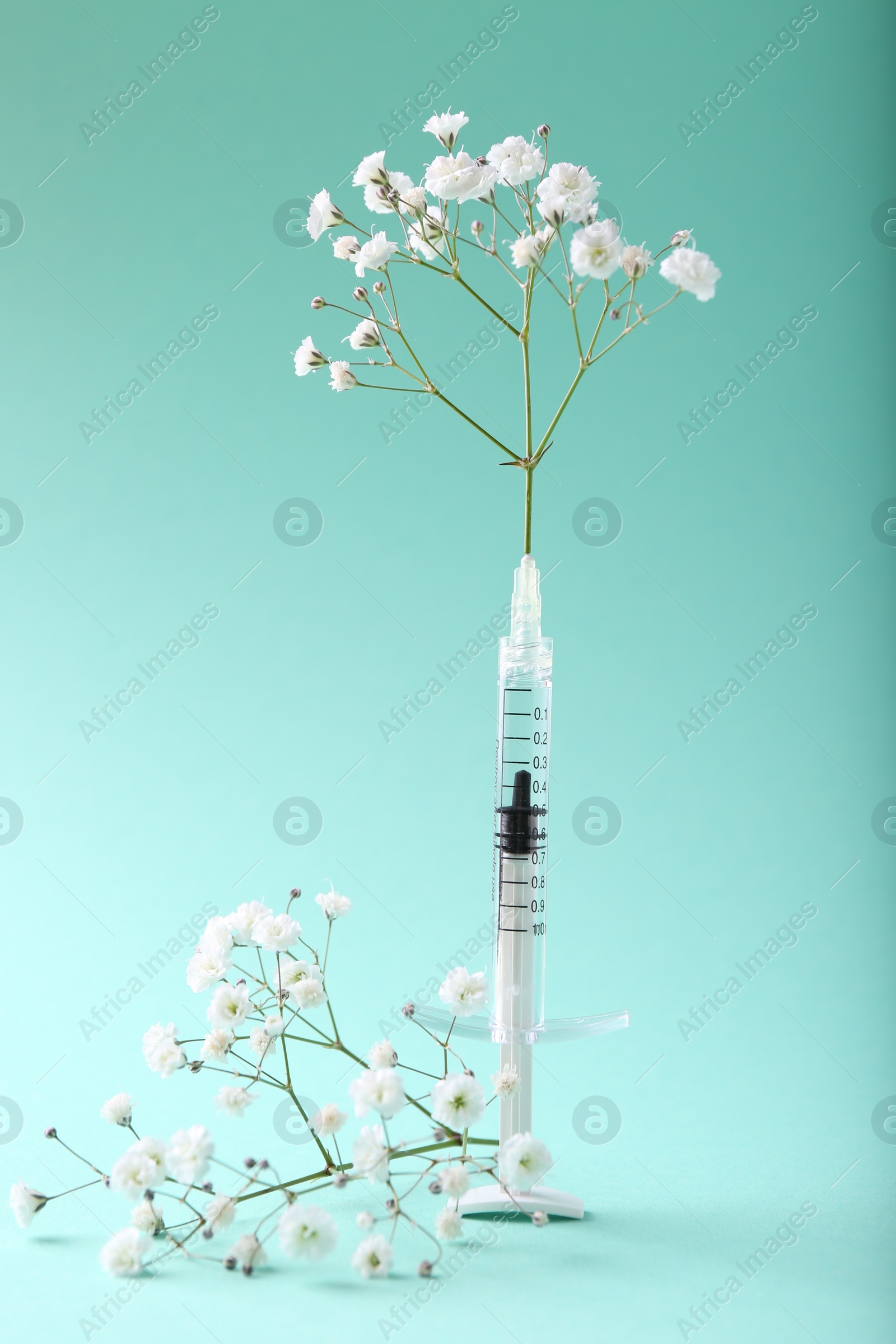 Photo of Cosmetology. Medical syringe and gypsophila flowers on turquoise background