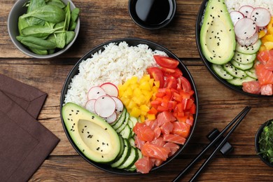 Delicious poke bowl with salmon and vegetables served on wooden table, flat lay