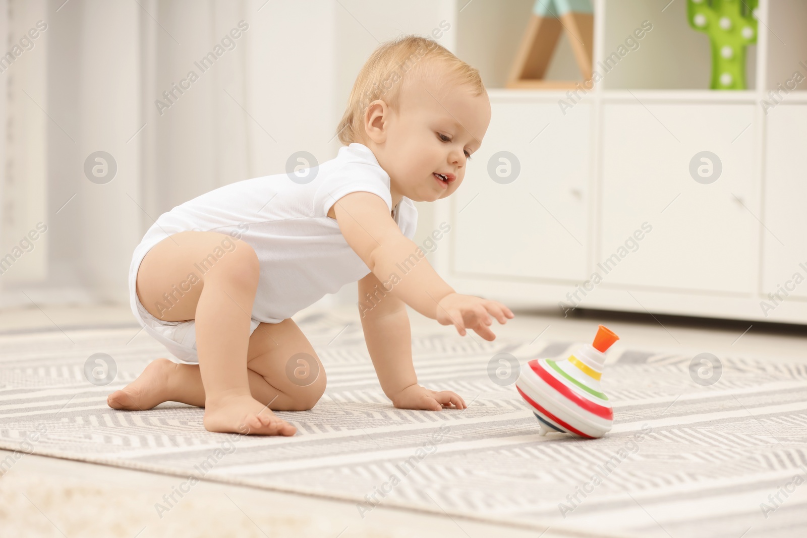 Photo of Children toys. Cute little boy playing with spinning top on rug at home
