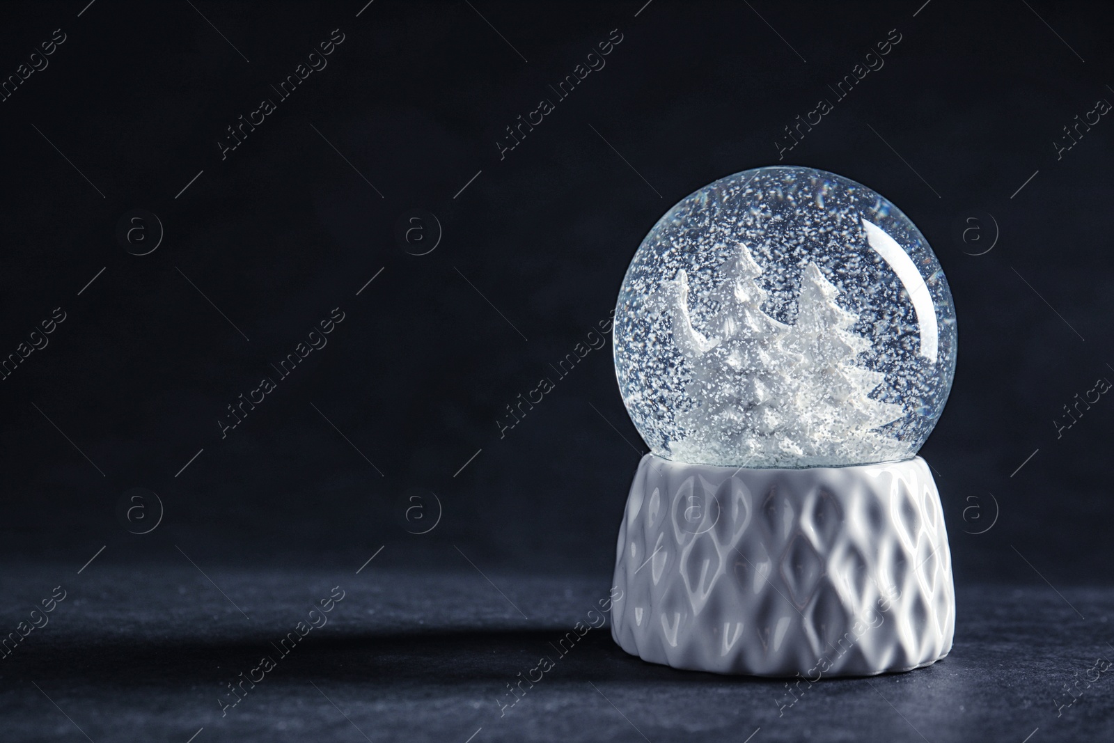 Photo of Snow globe with deer and trees on dark background. Space for text