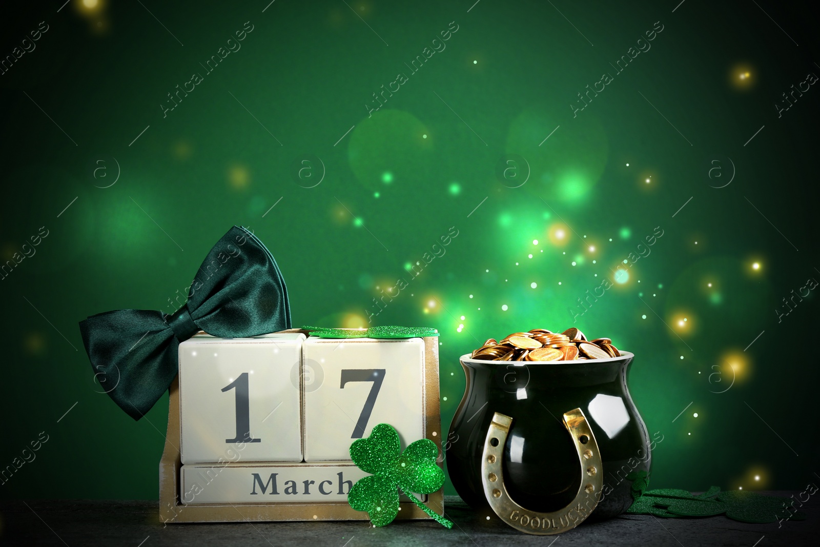 Image of Composition with pot of gold coins and wooden block calendar on grey stone table against green background. St. Patrick's Day celebration