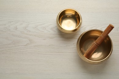 Photo of Golden singing bowls and mallet on white wooden table, flat lay. Space for text