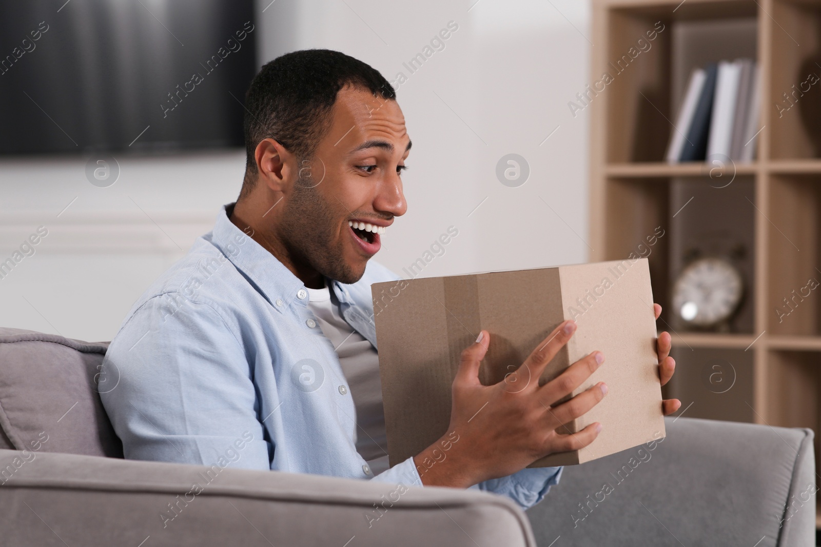 Photo of Emotional young man with parcel at home. Internet shopping