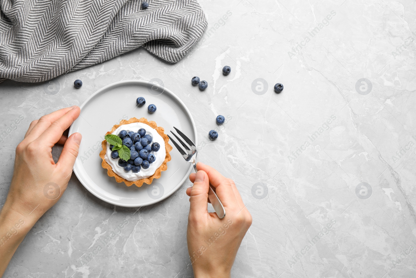 Photo of Woman eating blueberry tart at marble table, top view with space for text. Delicious pastries