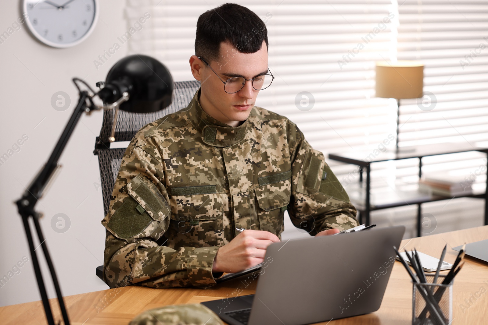 Photo of Military service. Young soldier working at wooden table in office