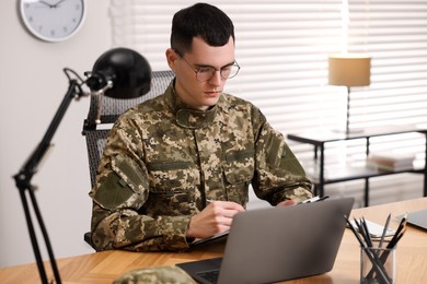 Military service. Young soldier working at wooden table in office