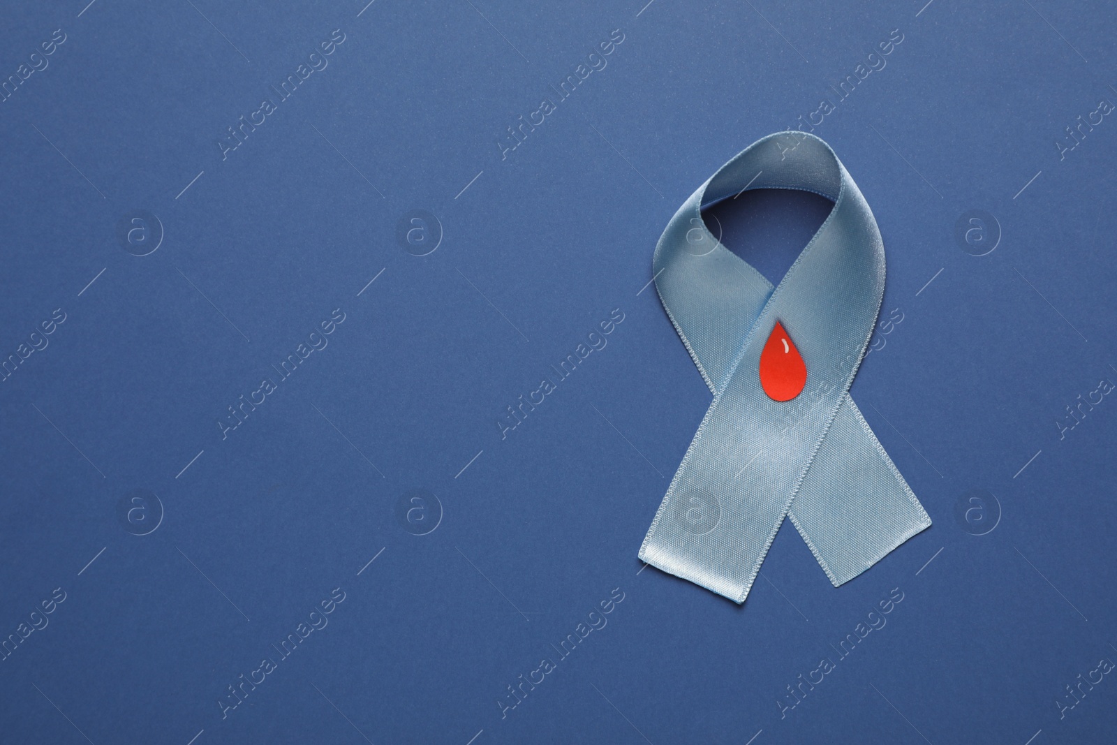 Photo of Light blue ribbon with paper blood drop on color background, top view and space for text. Diabetes awareness