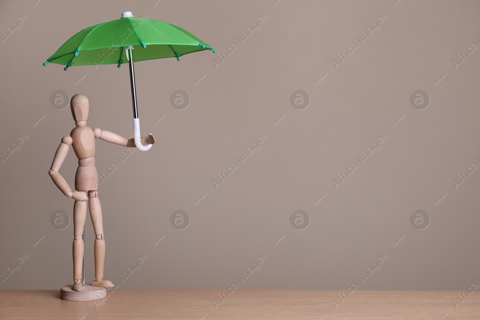 Photo of Mannequin holding small umbrella on wooden table. Space for text