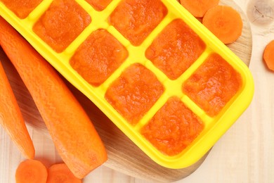 Carrot puree in ice cube tray and fresh carrot on wooden table, top view