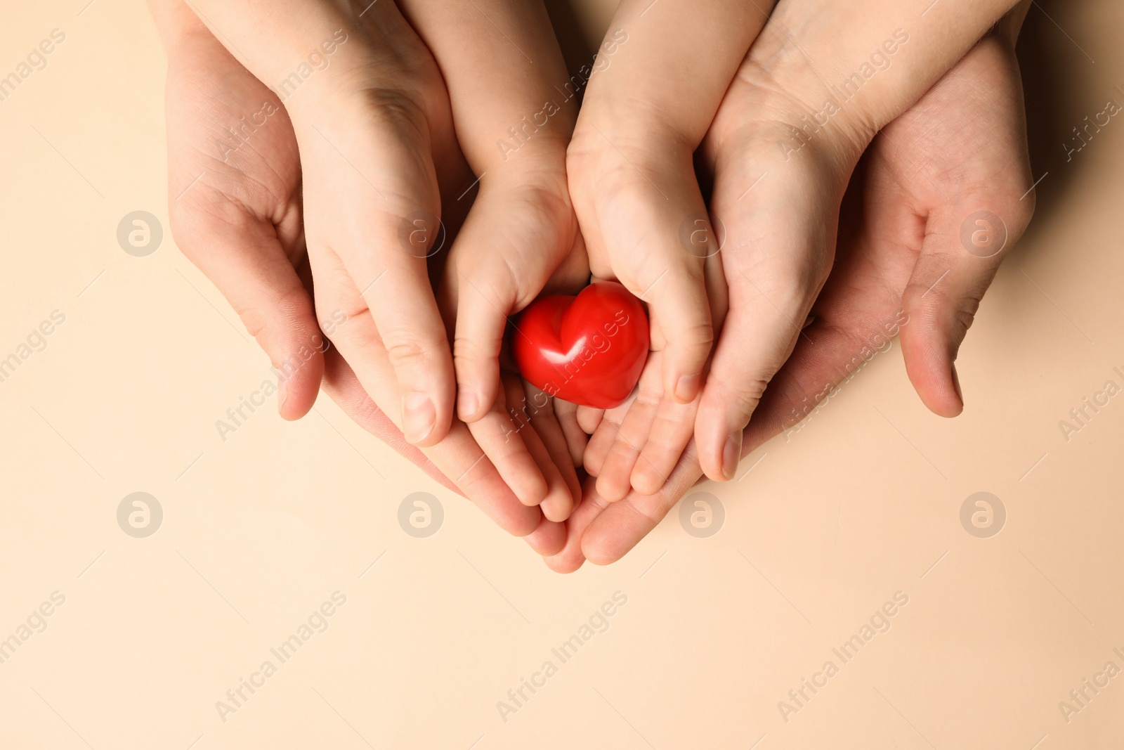 Photo of Parents and kid holding red heart in hands on beige background, top view