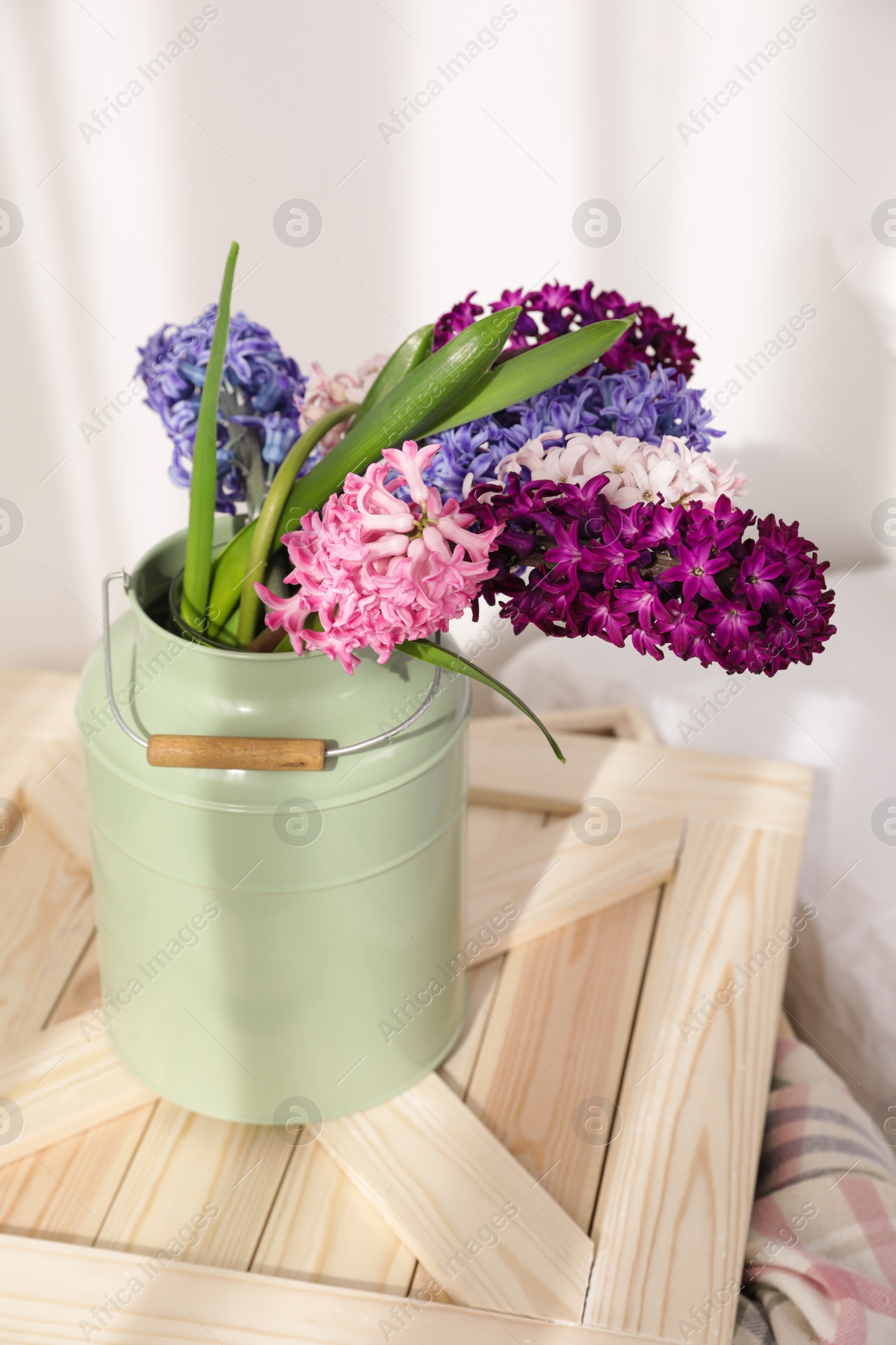 Photo of Beautiful hyacinths in metal can on wooden crate indoors. Spring flowers