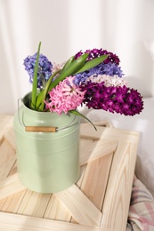 Photo of Beautiful hyacinths in metal can on wooden crate indoors. Spring flowers