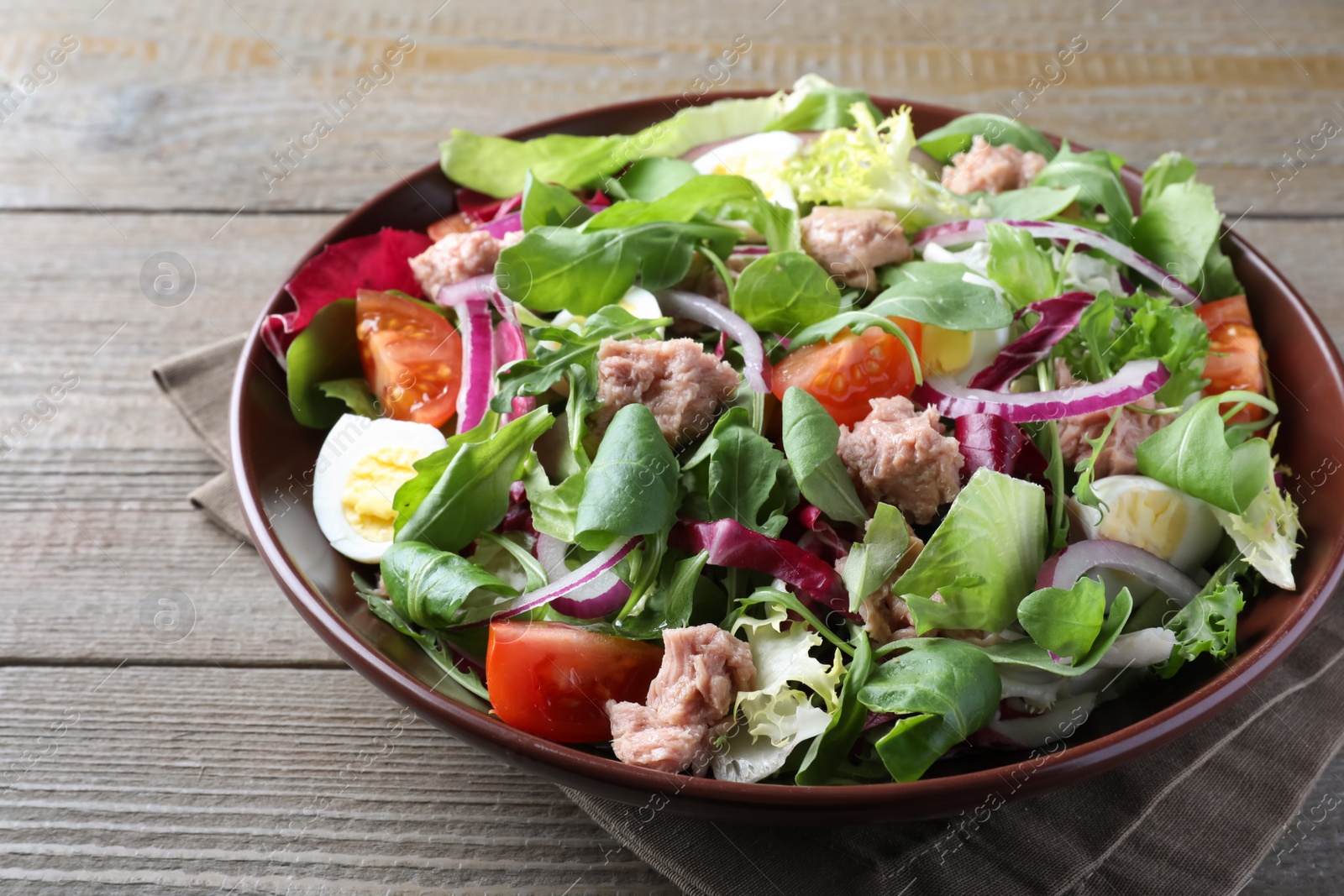 Photo of Bowl of delicious salad with canned tuna and vegetables on wooden table