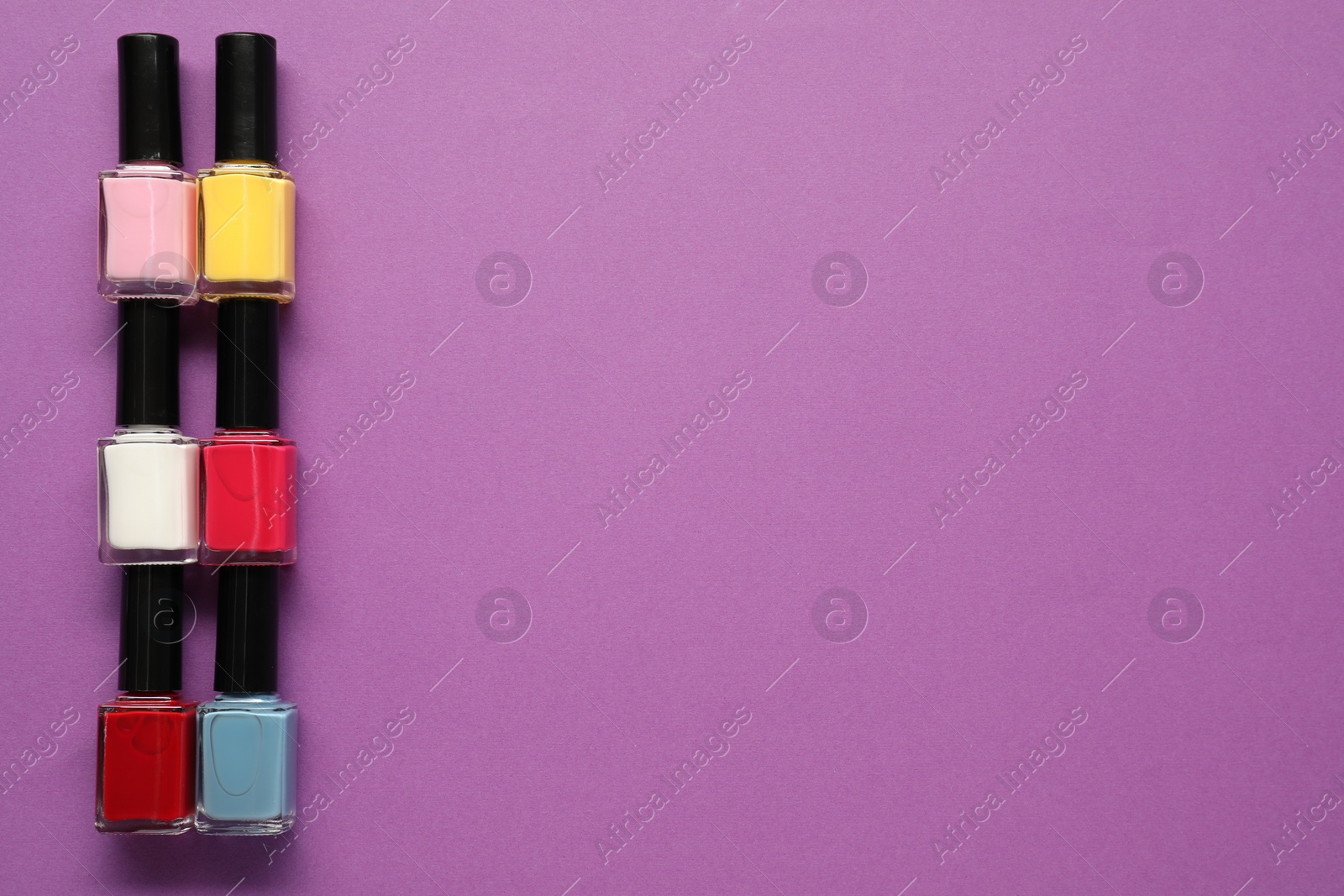 Photo of Bright nail polishes in bottles on purple background, flat lay. Space for text