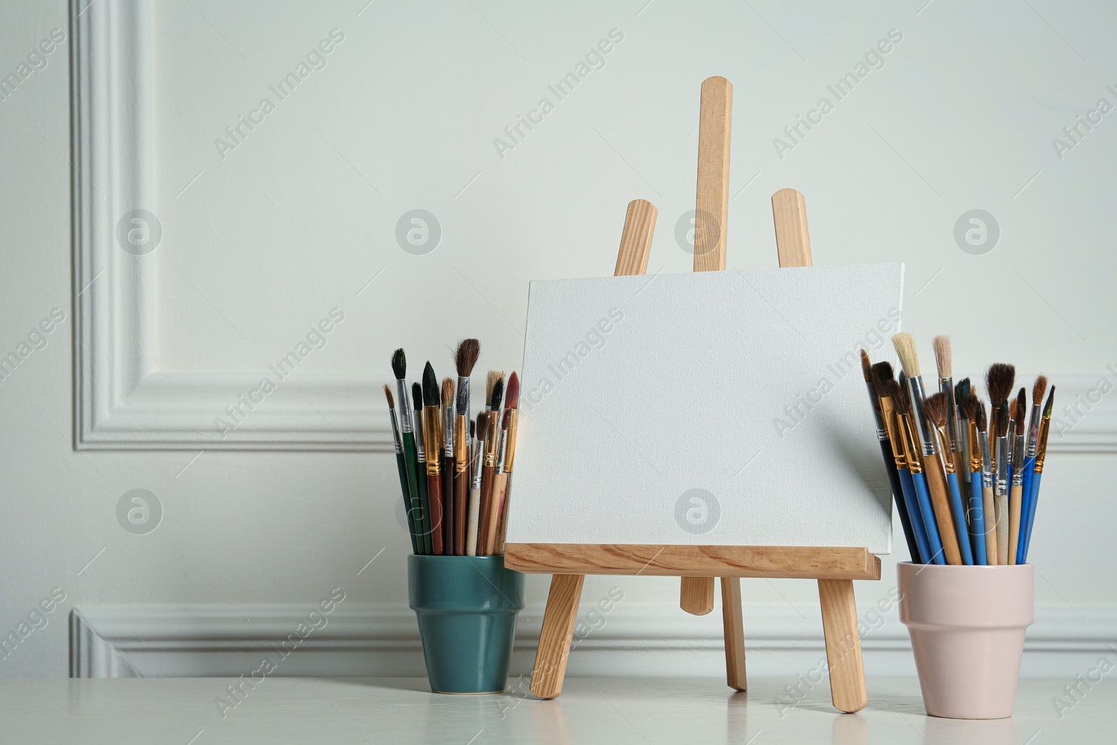 Photo of Easel with blank canvas and brushes on white wooden table