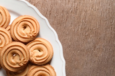 Photo of Plate with Danish butter cookies on wooden background, top view. Space for text