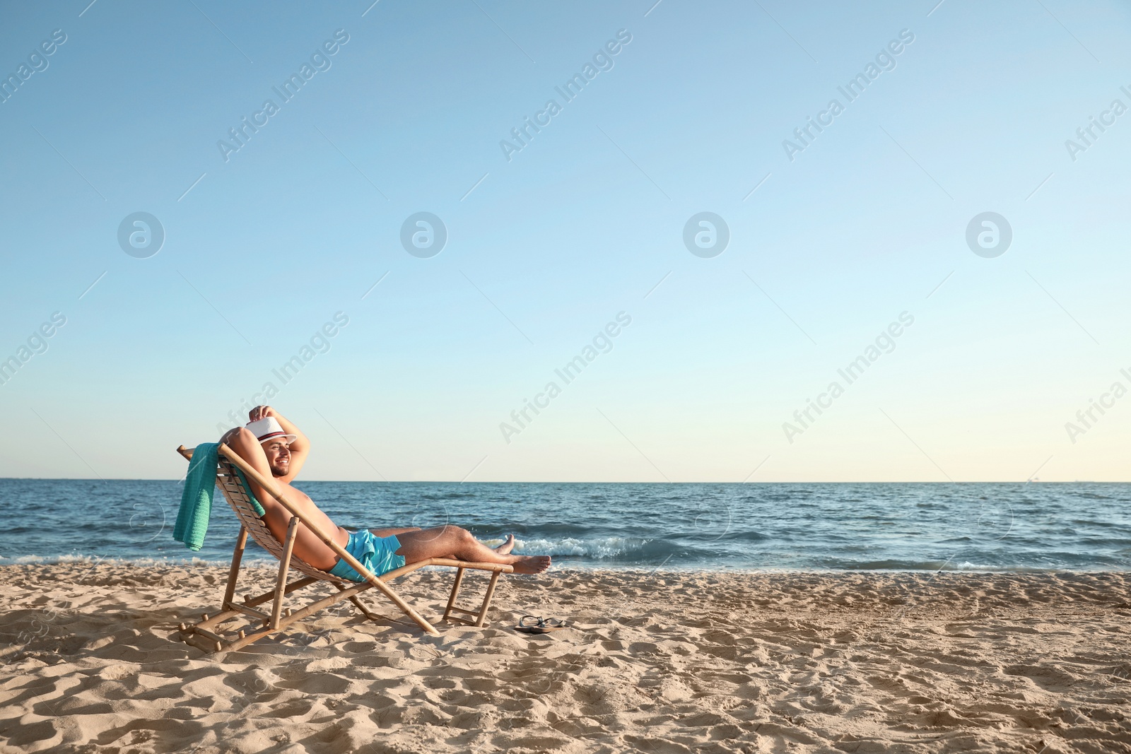 Photo of Young man relaxing in deck chair on beach near sea