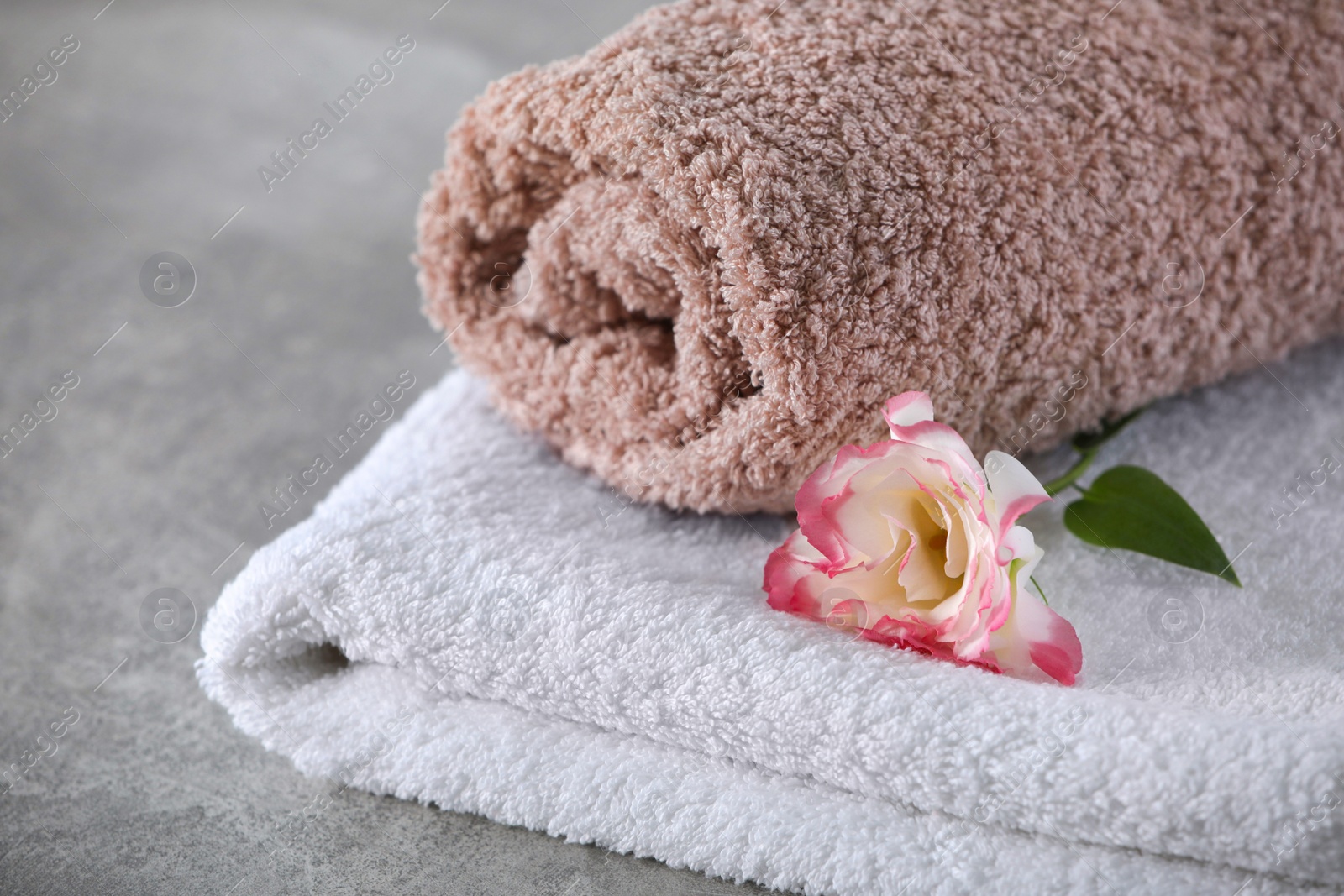 Photo of Soft towels with flower on grey table, closeup