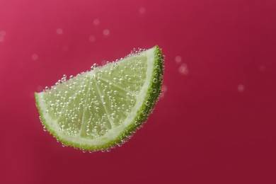 Photo of Slice of lime in sparkling water on dark pink background, space for text. Citrus soda