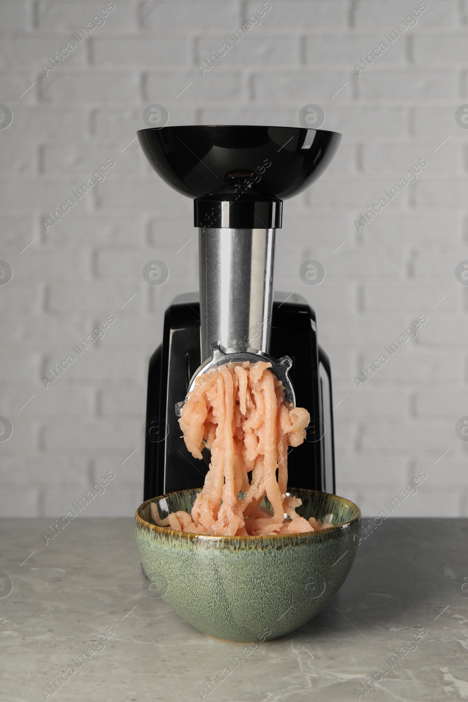 Photo of Electric meat grinder with chicken mince on grey marble table near white wall