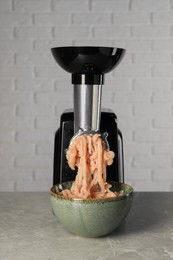 Electric meat grinder with chicken mince on grey marble table near white wall