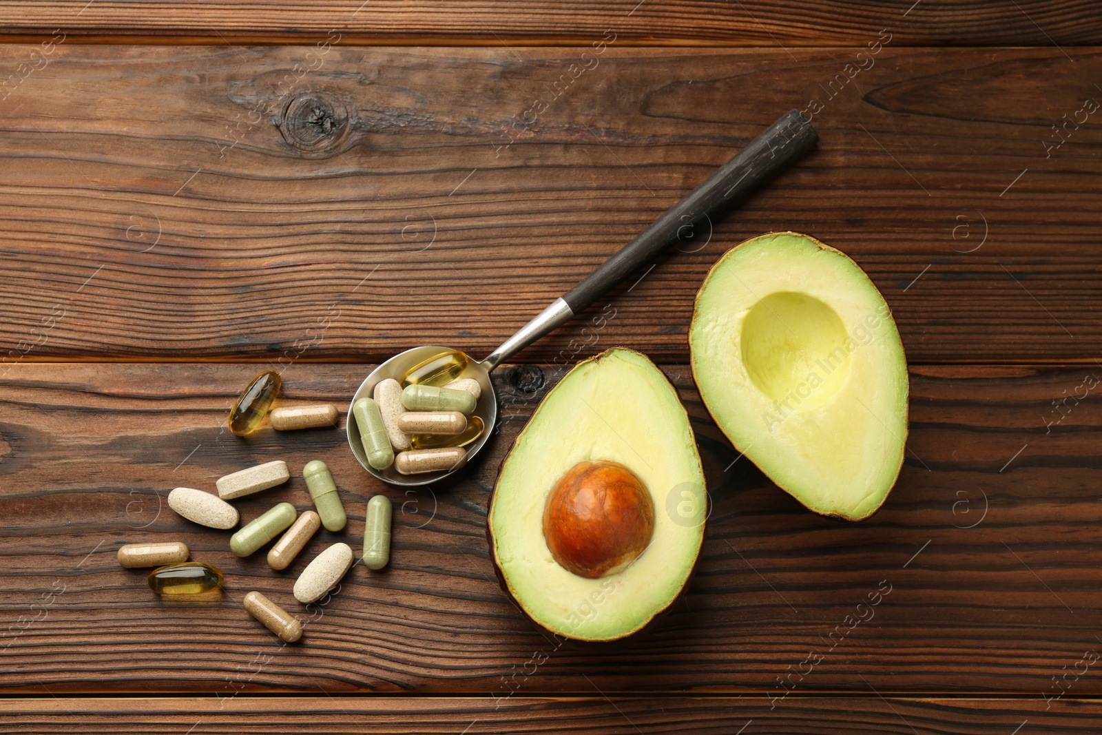 Photo of Different vitamin pills and avocado on wooden table, flat lay