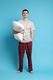 Happy man in pyjama holding pillow on light blue background