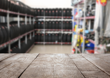 Image of Empty wooden surface and blurred view of car tires in auto store, closeup. Space for text 