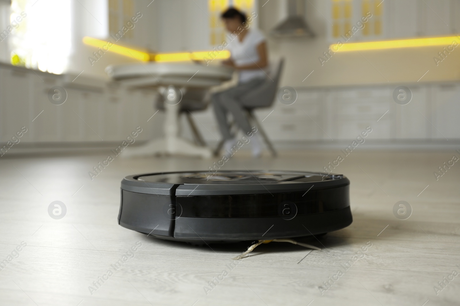 Photo of Modern robotic vacuum cleaner and blurred woman on background