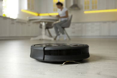 Modern robotic vacuum cleaner and blurred woman on background