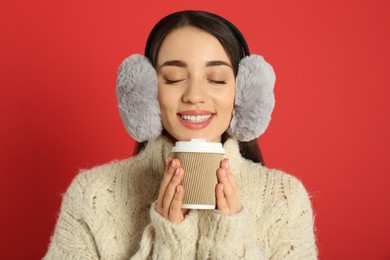 Photo of Beautiful young woman in earmuffs with cup of drink on red background